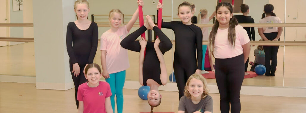 Kids at an aerial acrobatics group activity, with red hammocks/silks.